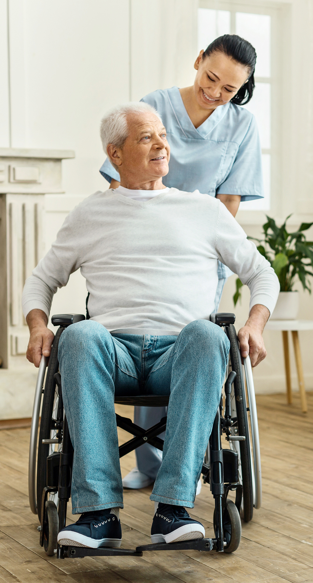 Senior man in wheelchair being pushed by nurse caregiver in his home