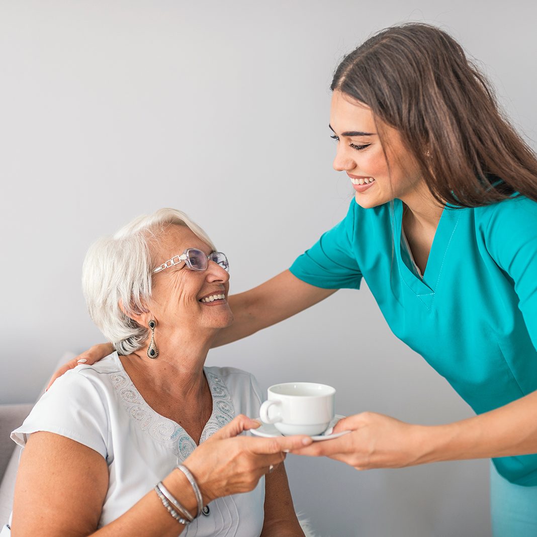 provider hands senior woman a cup of tea