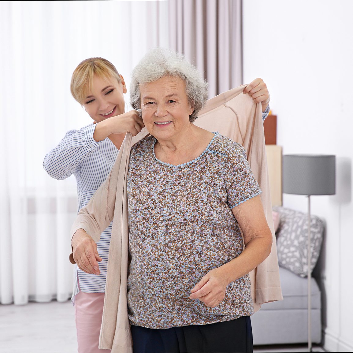 care provider helping senior woman put on a cardigan